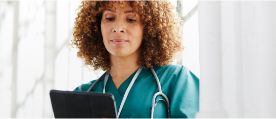 Woman with brown curly hair and in medical attire looking down at ipad